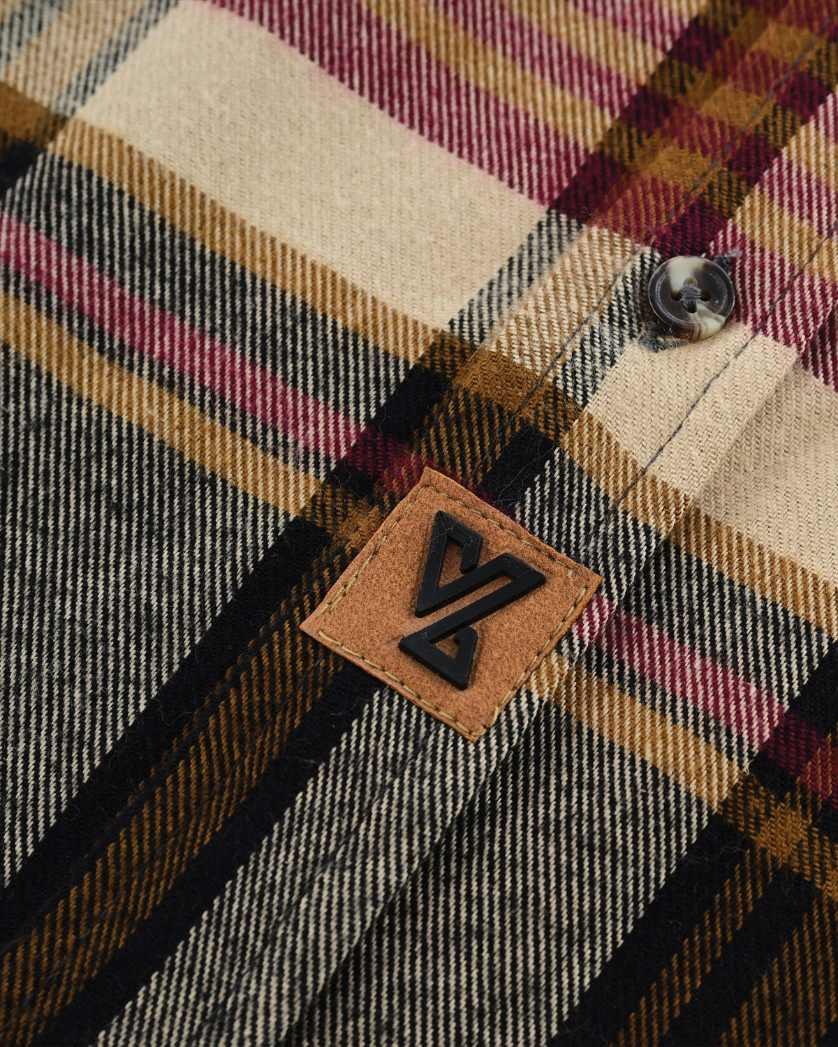 Close-up of the Vance logo patch beside the button placket on maroon, beige and charcoal Cedarwood Plaid cotton flannel.