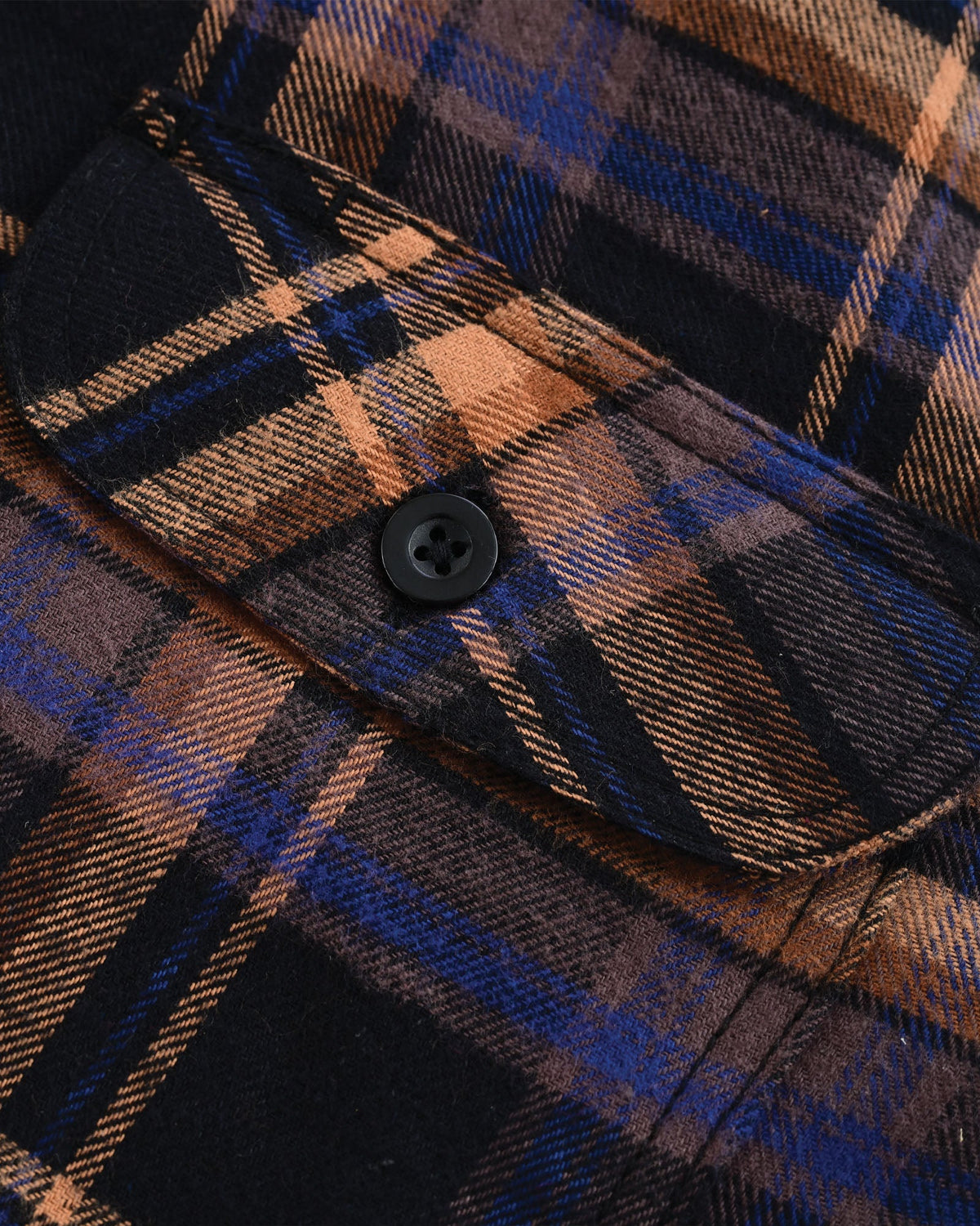 Close-up of a Midnight Rust plaid flannel chest pocket with an angled flap, black button and stitched edges.