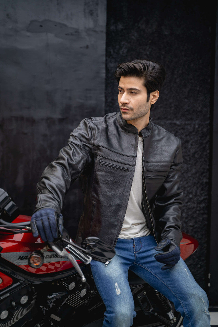 Man wearing a black leather cafe racer motorcycle jacket and gloves while seated on a red motorcycle.