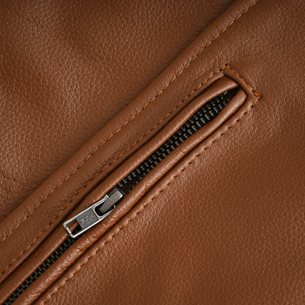 Close-up of a YKK zippered waist pocket with stitched leather welting on the brown cowhide motorcycle jacket.