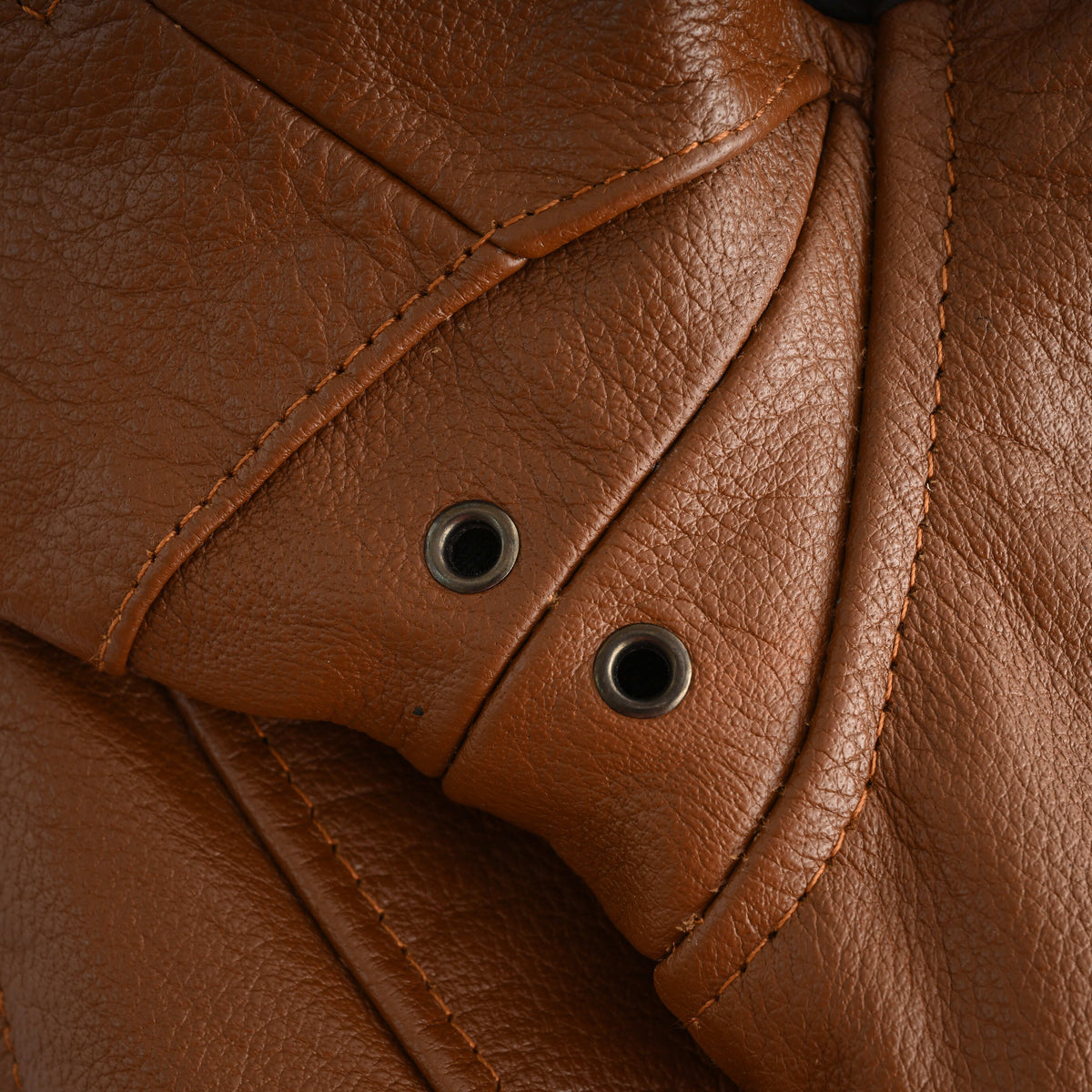 Close-up of two metal ventilation eyelets beneath the arm of the brown cowhide leather motorcycle jacket.