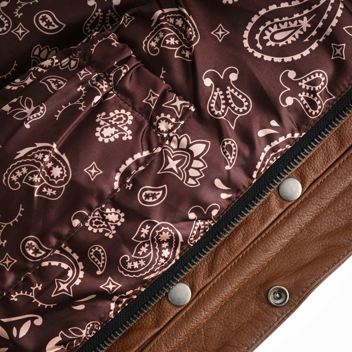 Close-up of the motorcycle vest's brown paisley interior, showing pocket stitching beside the zipper and leather snap placket.