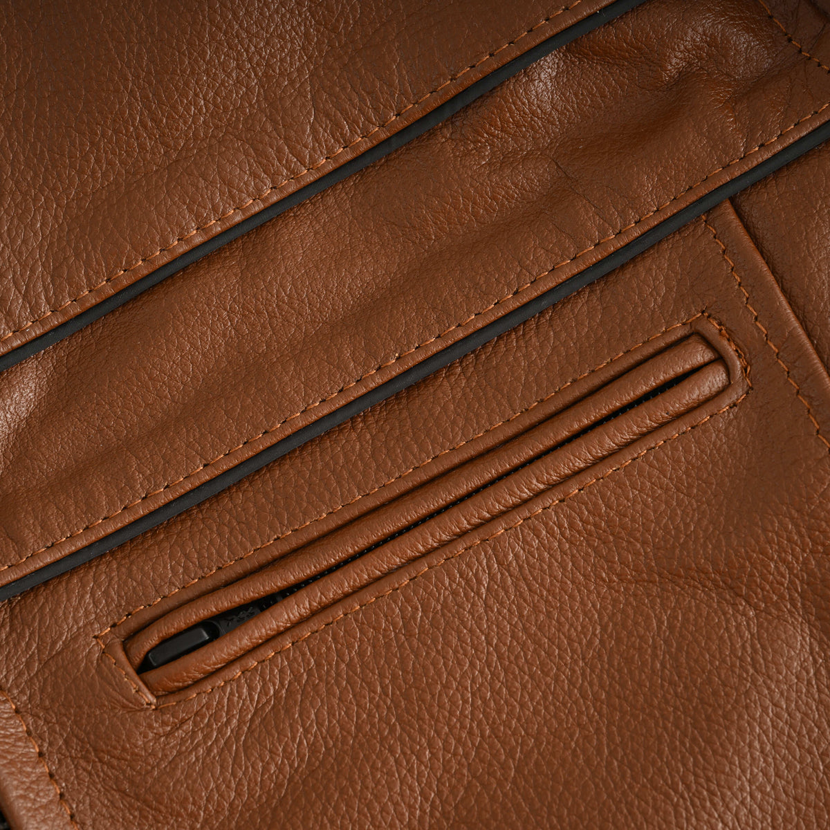 Close-up of twin black racing piping lines above a horizontal chest zipper on the cognac cowhide cafe racer jacket.