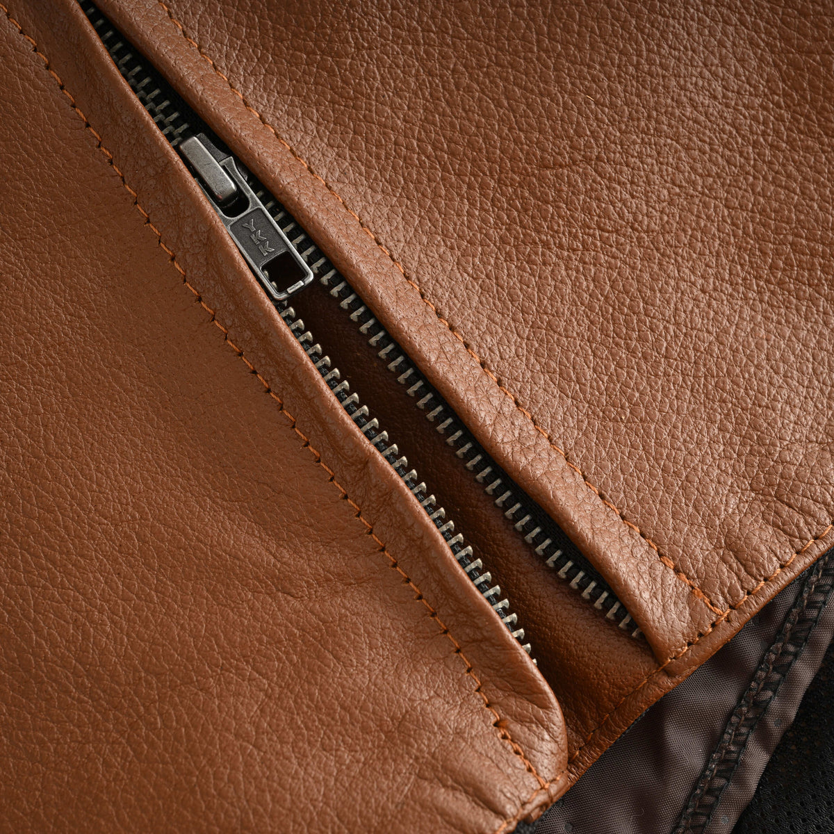 Close-up of the cognac motorcycle jacket's side waist zipper opened to reveal its expandable leather gusset.