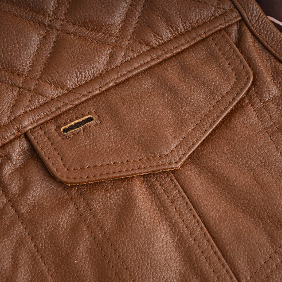 Close-up of the cognac leather vest's chest pocket flap with a sunglass holder slot beneath the diamond-quilted yoke.