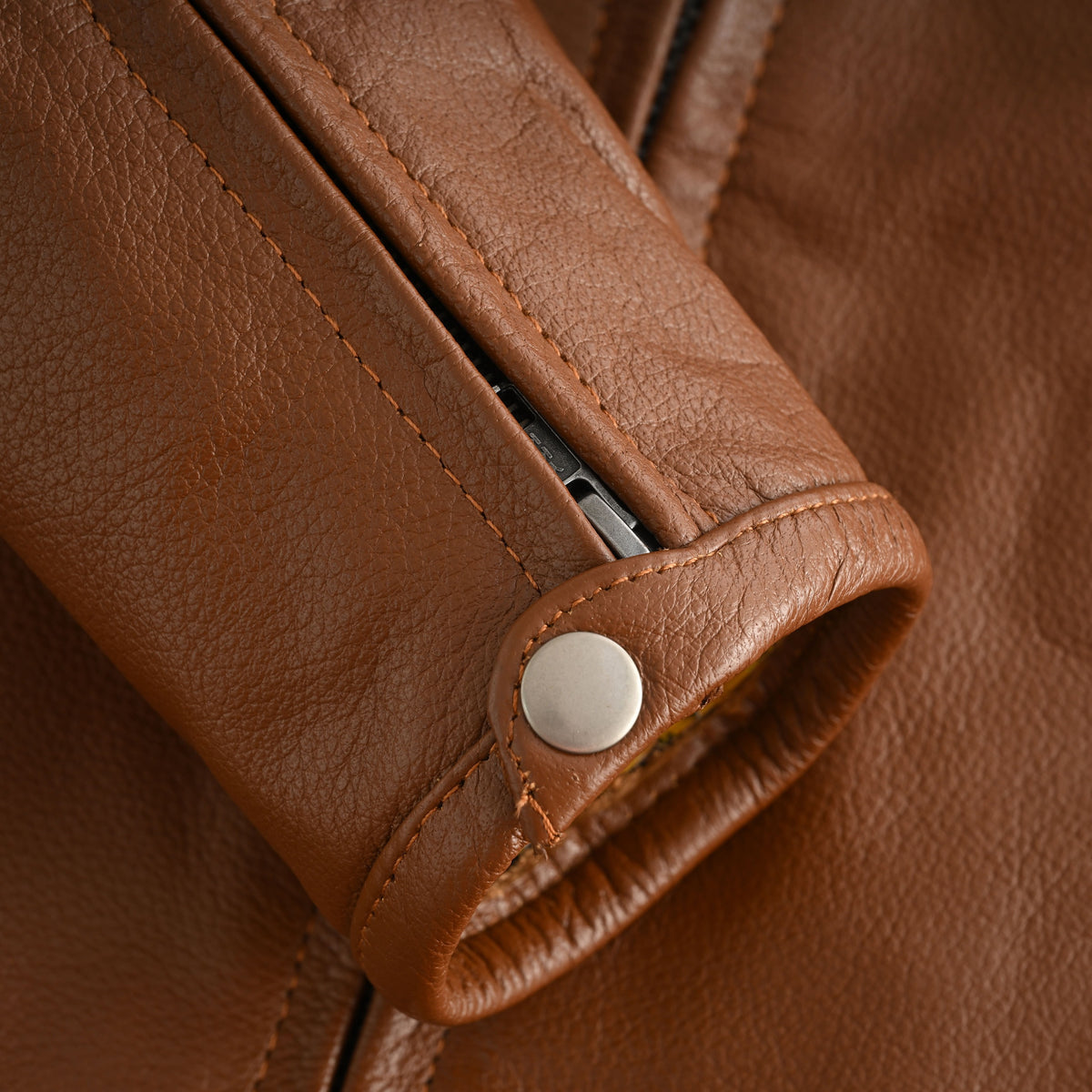 Close-up of the cognac leather cafe racer jacket's zippered sleeve cuff with a leather snap tab and metal fastening.