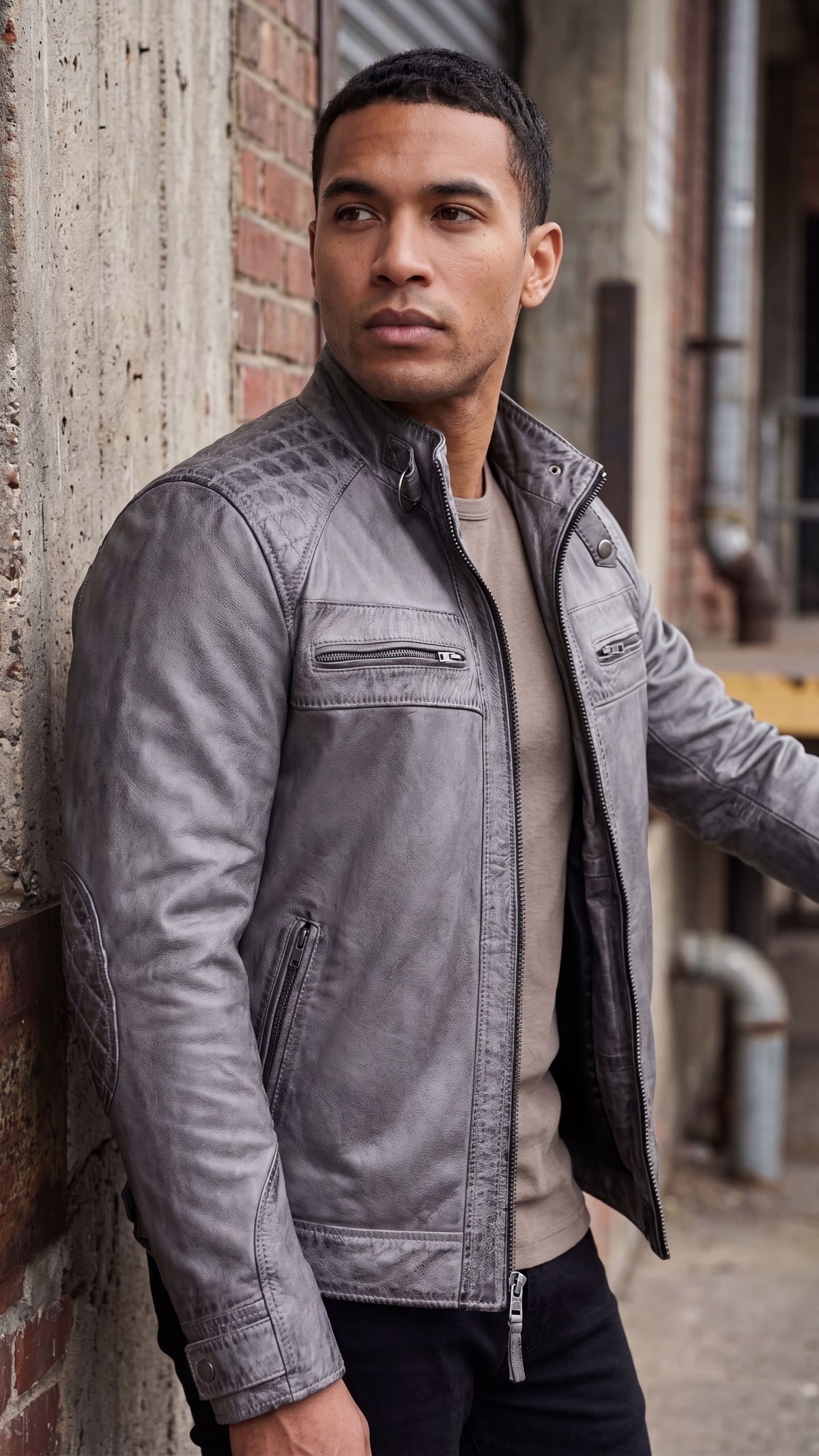 Man leaning against a brick wall in a distressed grey leather cafe racer jacket with quilted shoulders and a snap collar.
