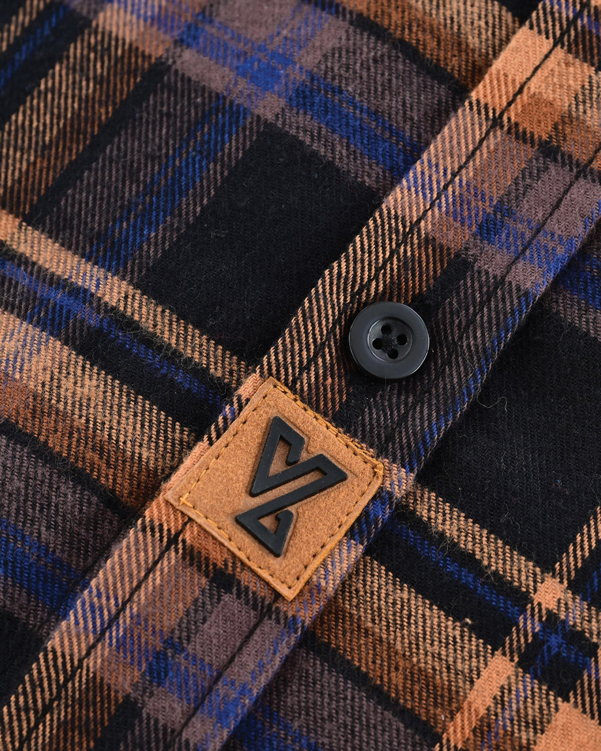 Vance logo patch beside a black button on the Midnight Rust flannel shirt's navy, brown and rust plaid fabric.